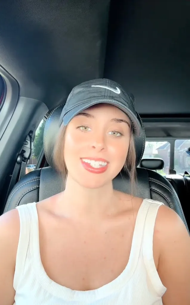 Christina Hart, a TikTok food critic, sitting in a car and smiling while wearing a Nike cap.