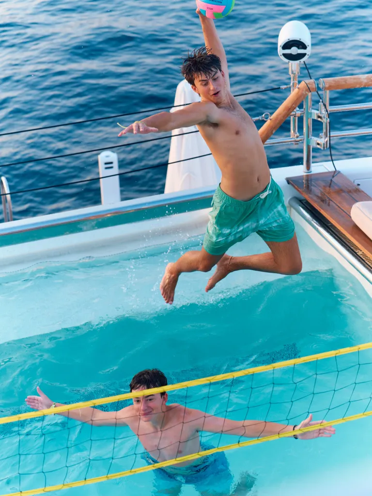 Two boys playing volleyball in a pool on a yacht.
