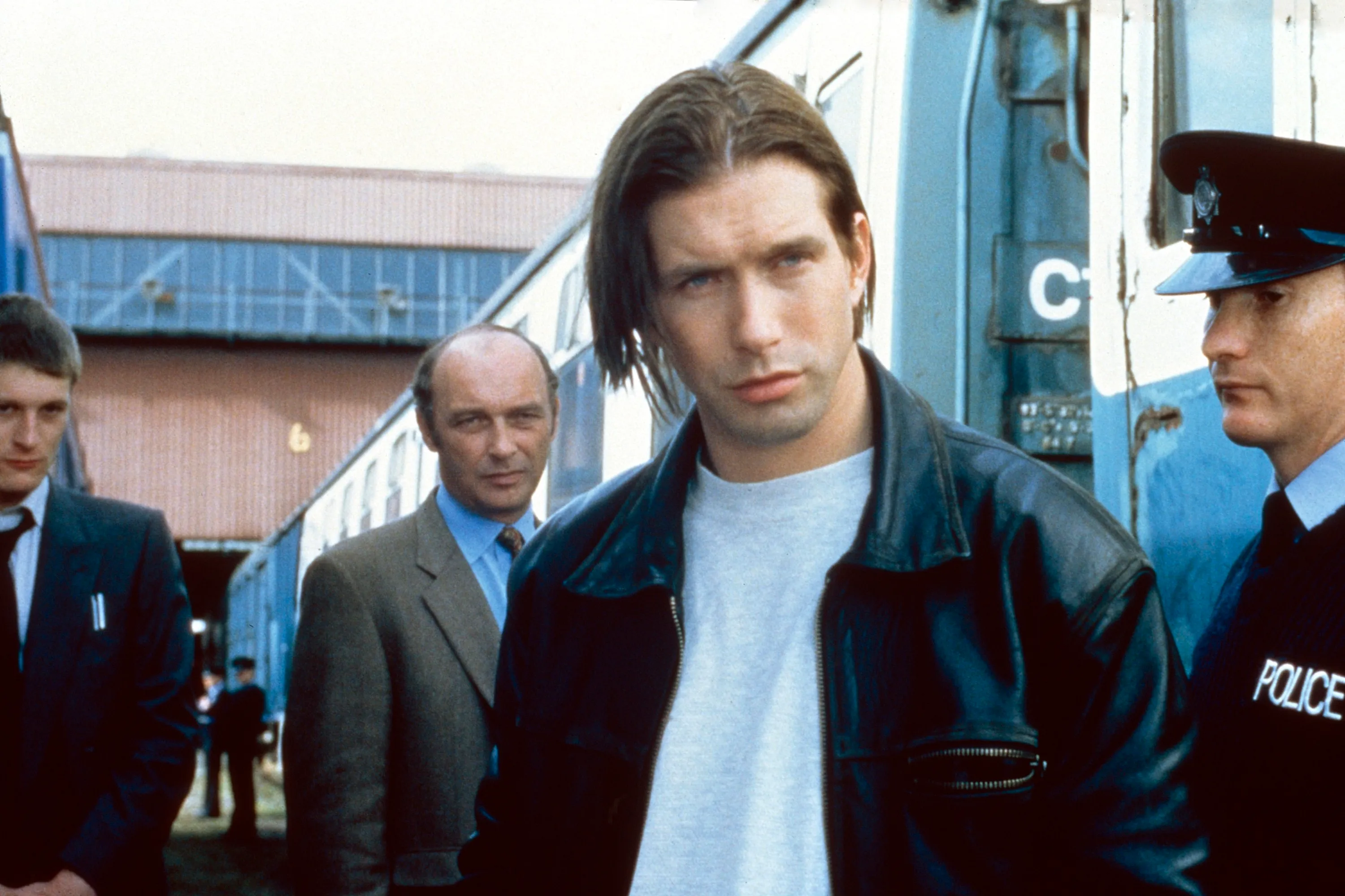 Stephen Baldwin in a leather jacket and t-shirt, next to a police officer and two men in suits, in a scene from the film Crimetime.