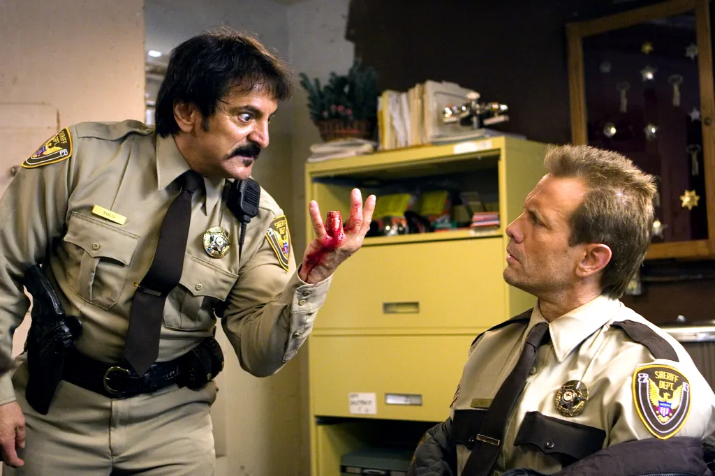 Two policemen in uniform, one showing the other his bloody, severed finger.
