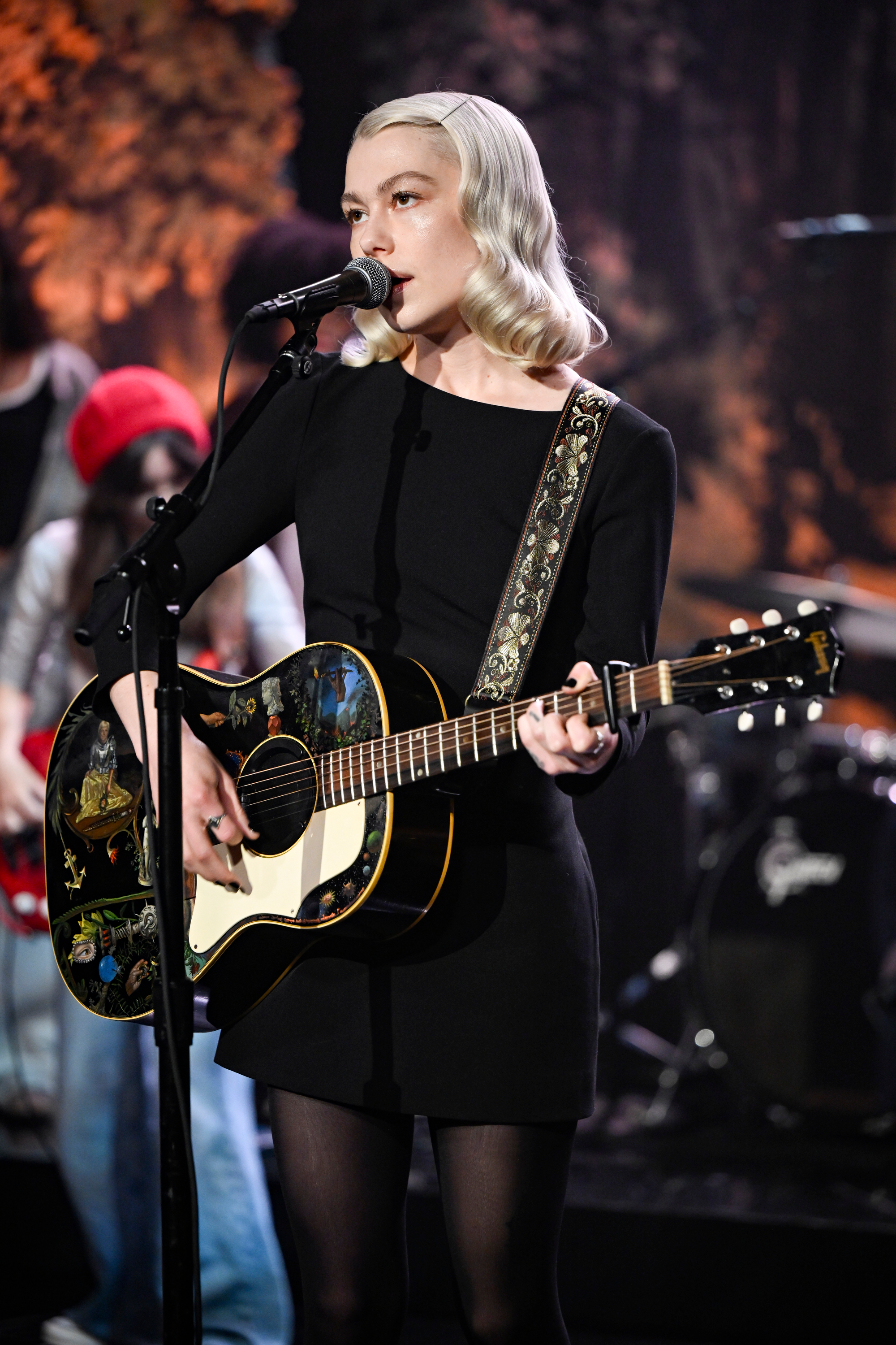 Phoebe Bridgers playing guitar and singing into a microphone on stage.