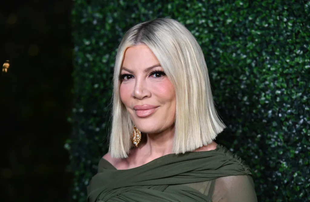 Tori Spelling in a dark green dress and gold earrings.