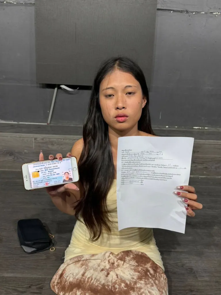 A young woman holding up a Thai ID card displayed on a phone and a paper document.