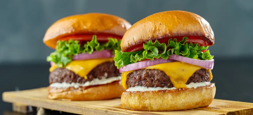 Two beefy cheeseburgers with American cheese, lettuce, tomato, and onion.