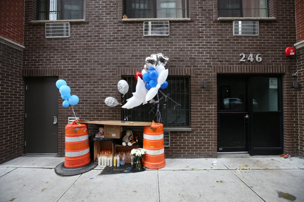 A makeshift memorial with balloons, candles, and stuffed animals sits outside a brick apartment building at 246 Echo Place.