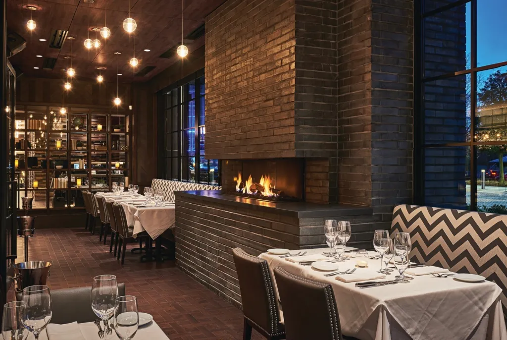 Dining room of Steak 48 restaurant with brick walls, fireplaces, and tables set for dinner.