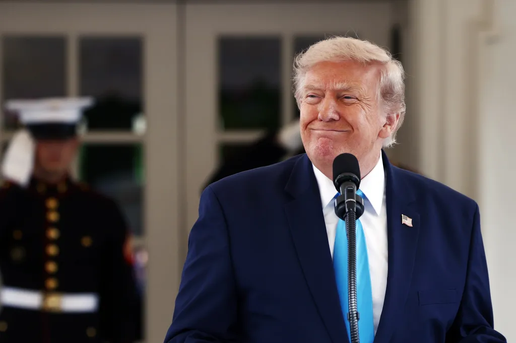 Donald Trump speaking at a podium with a US Marine in the background.
