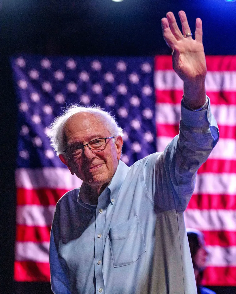 Bernie Sanders waving with an American flag in the background.