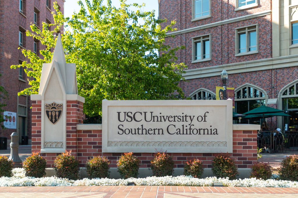 A stone sign for the University of Southern California (USC) with a brick base and surrounding foliage.