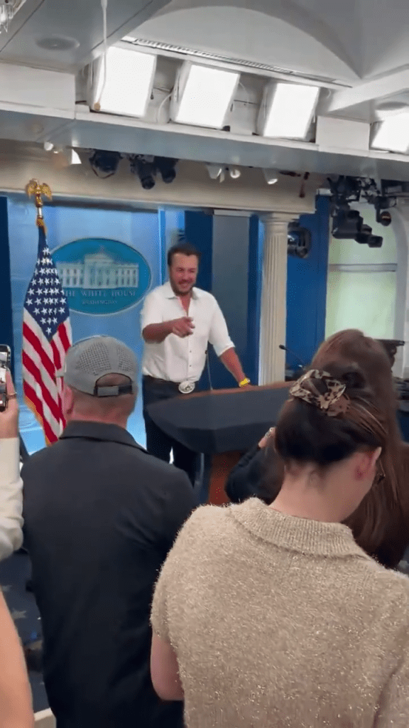 Bryan behind a White House press conference podium, pointing and smiling.