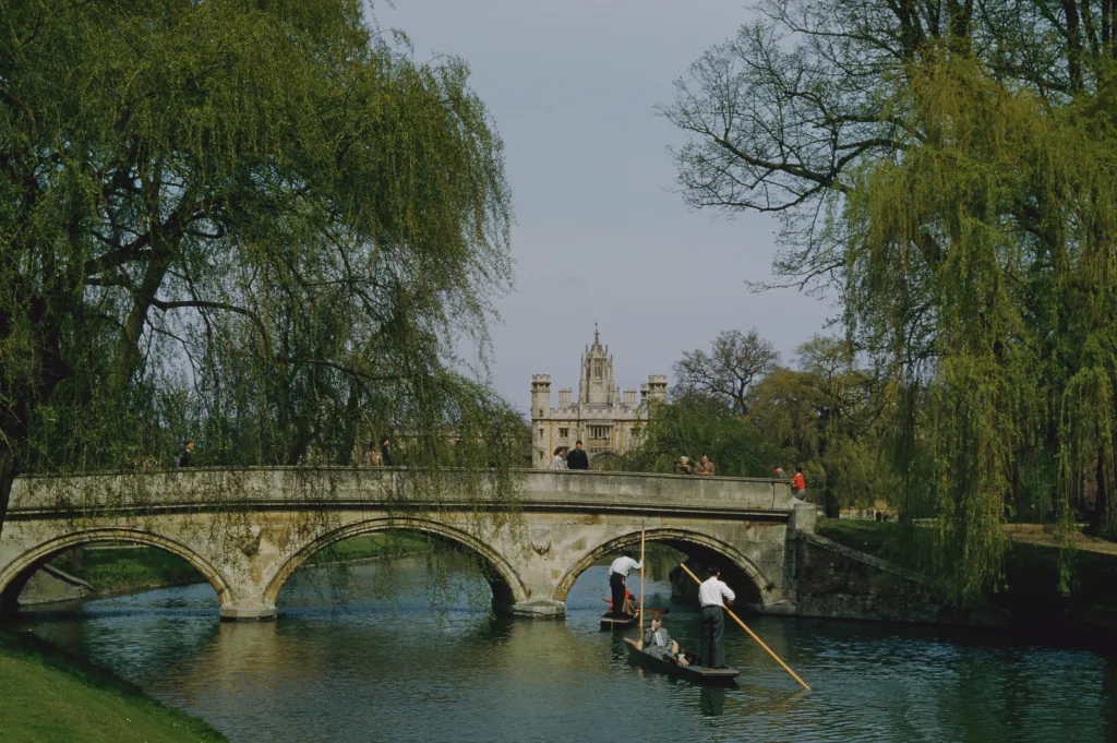 View across the River Cam towards St John's College, Cambridge with people punting and on a bridge.