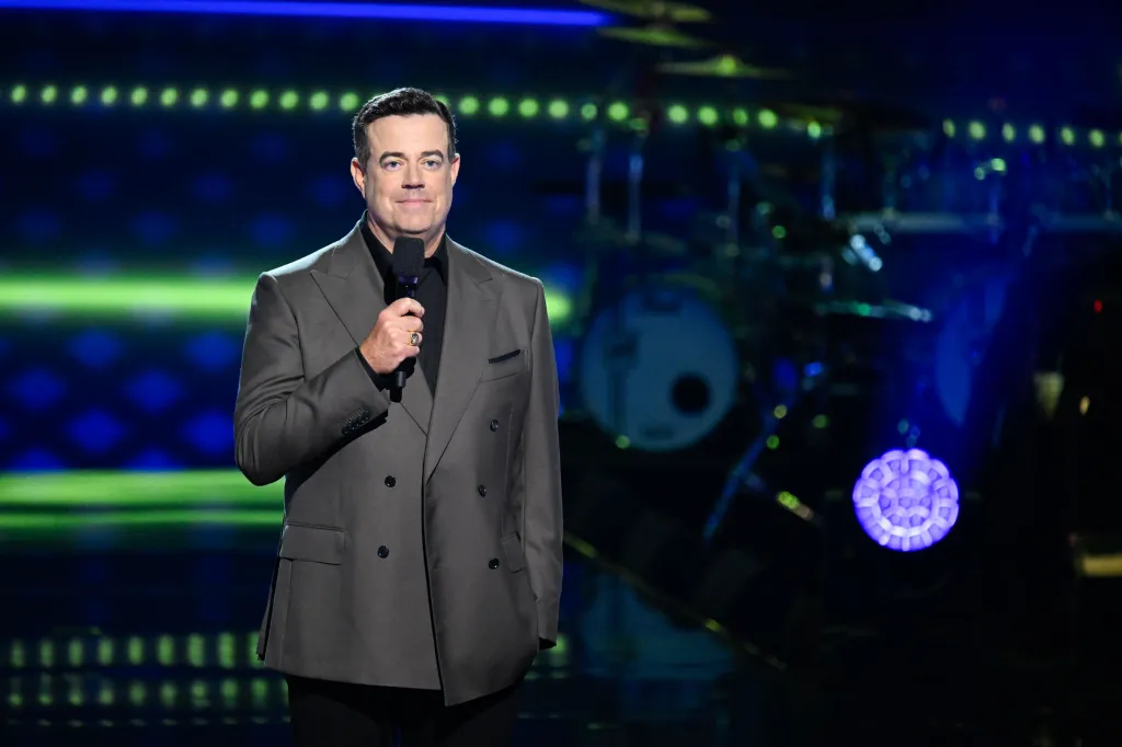 Carson Daly, host of The Voice, holding a microphone.