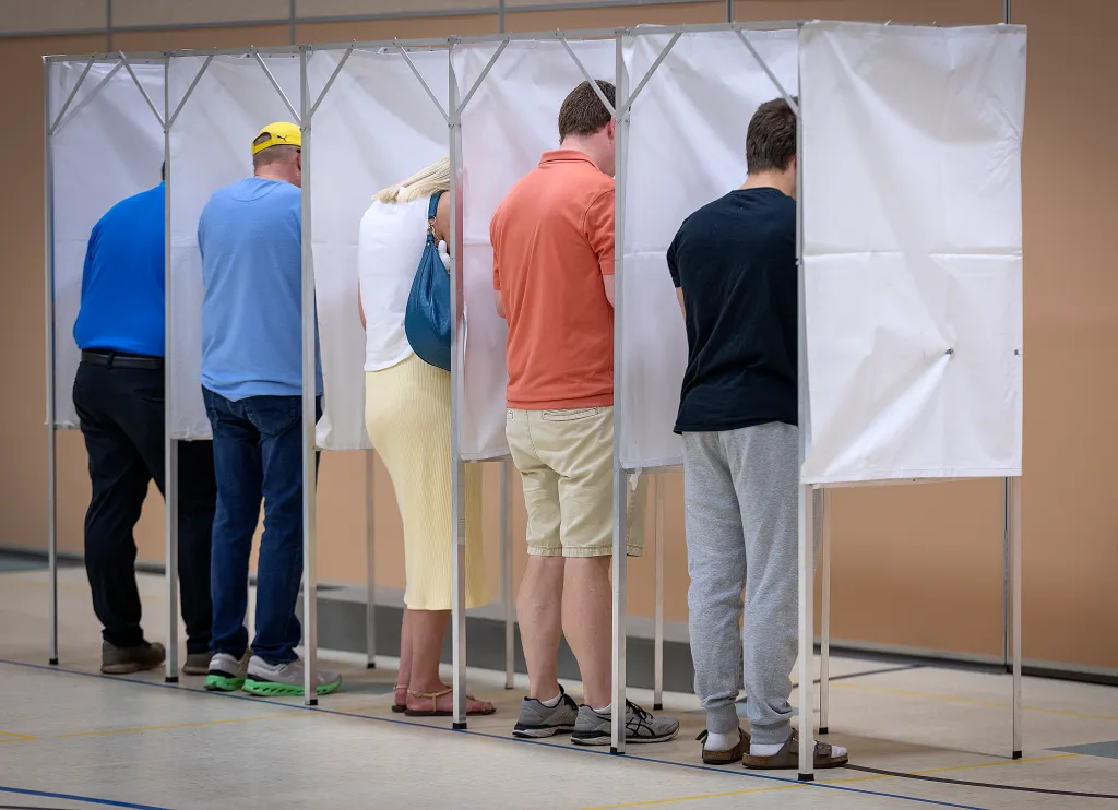 Five voters casting ballots in individual booths.