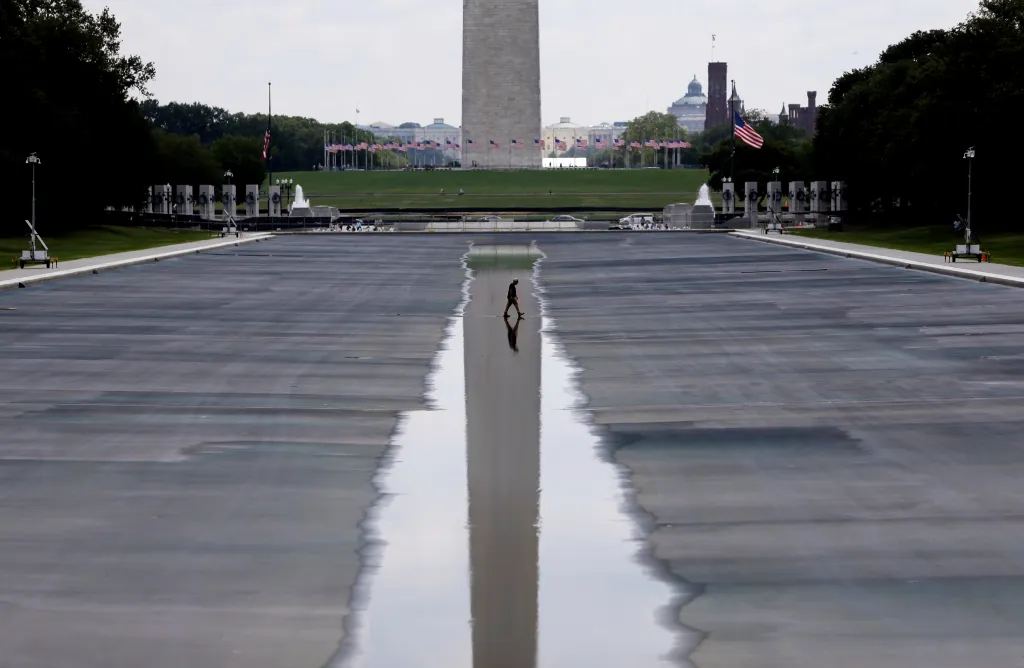 A person walks across the partially drained Lincoln Memorial Reflecting Pool with the Washington Monument in the background.