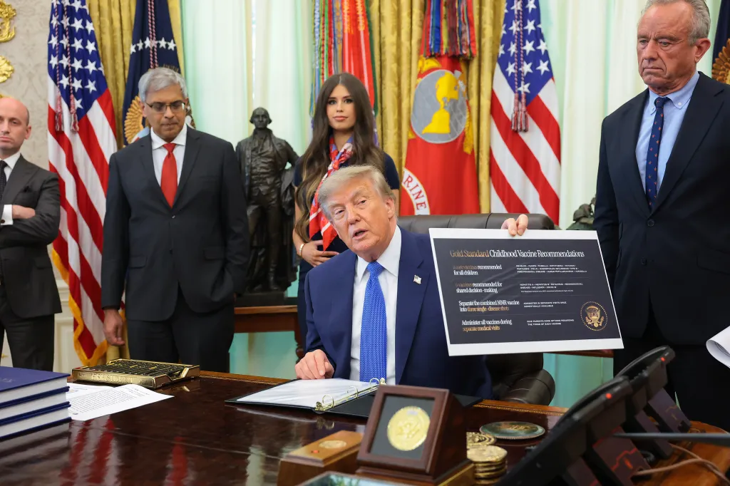Trump, accompanied by (L-R) White House Deputy Chief of Staff and Homeland Security Advisor Stephen Miller, National Institutes of Health Director Jay Bhattacharya, Jayme Leagh Franklin with the The Conservateur, and Health and Human Services Secretary Robert F. Kennedy Jr., holds up a sign that reads