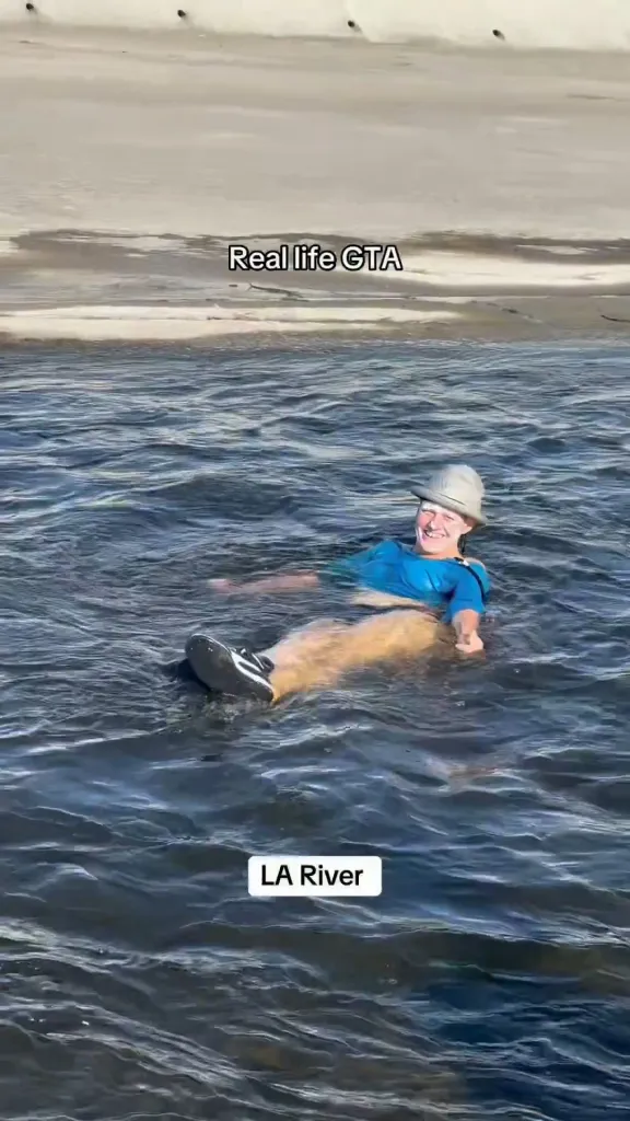 A woman in a blue shirt and hat floats on her back in the Los Angeles River.