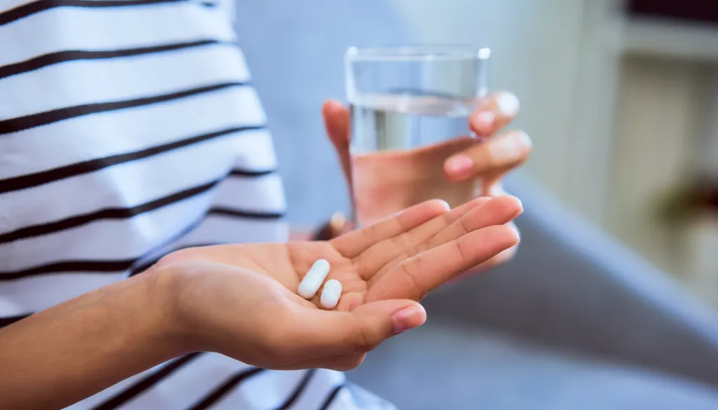 Woman holding a white pill and a glass of water.