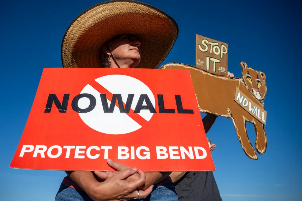 A woman in a straw hat holds a red sign that reads 