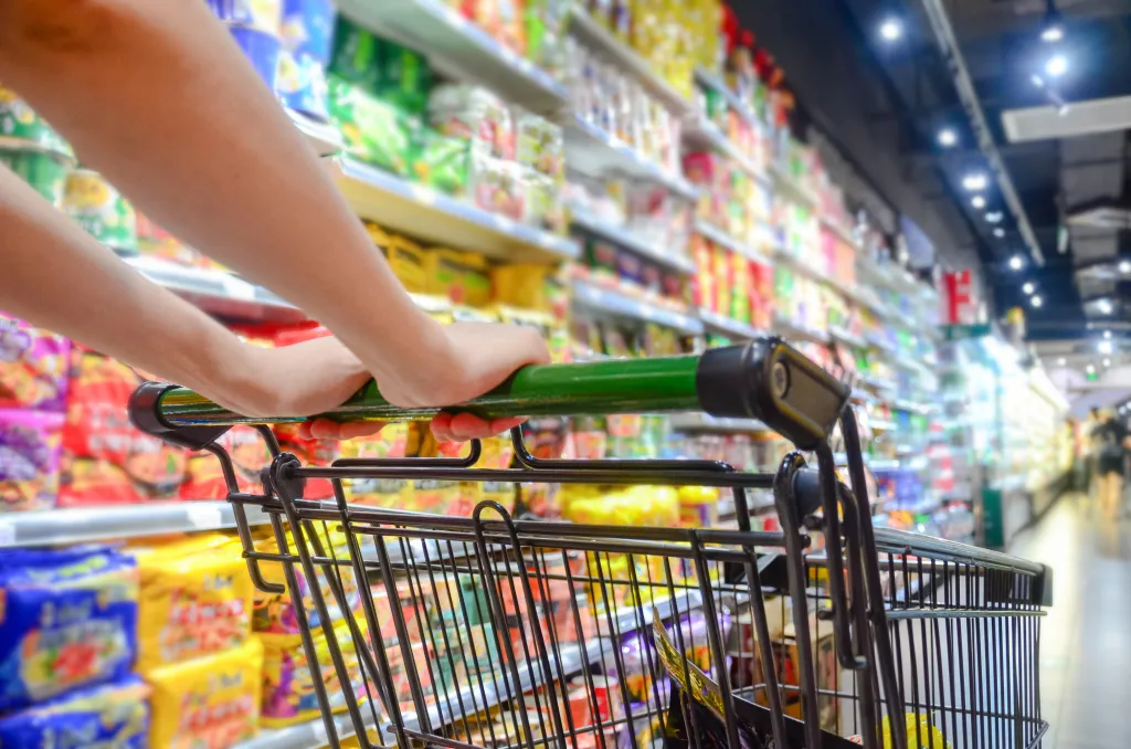 A woman pushes a shopping cart down a grocery store aisle.
