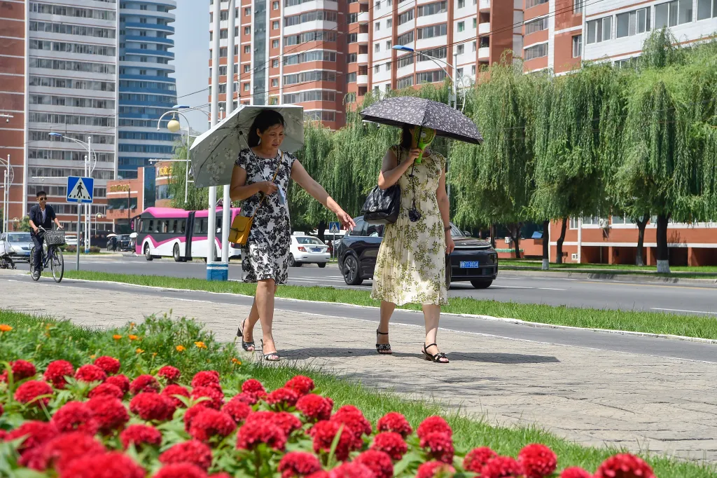 Two women walk along a street in Pyongyang, North Korea, using umbrellas to shield themselves from the sun.