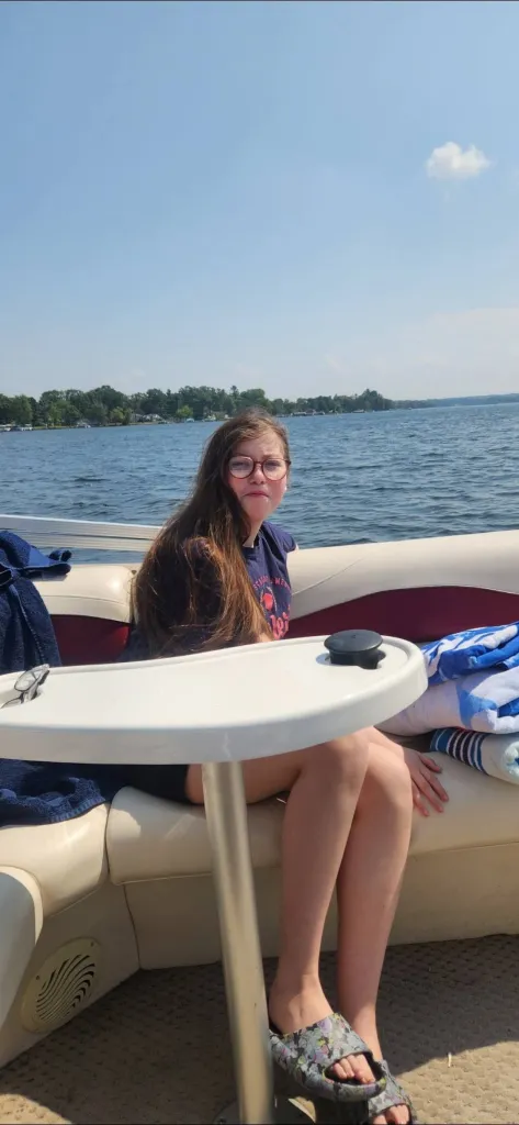 Bella, a young girl, sits on a boat in a lake with her brown hair flowing over her shoulders.