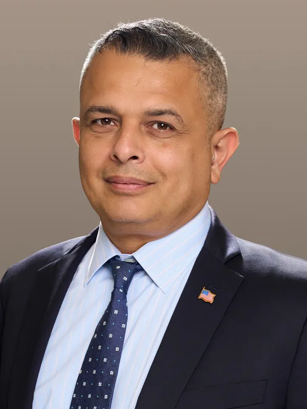 Andres Gil, a man in a suit and tie with an American flag lapel pin.