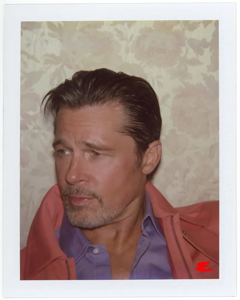 A polaroid photo of Brad Pitt in a pink jacket and purple shirt, looking left.