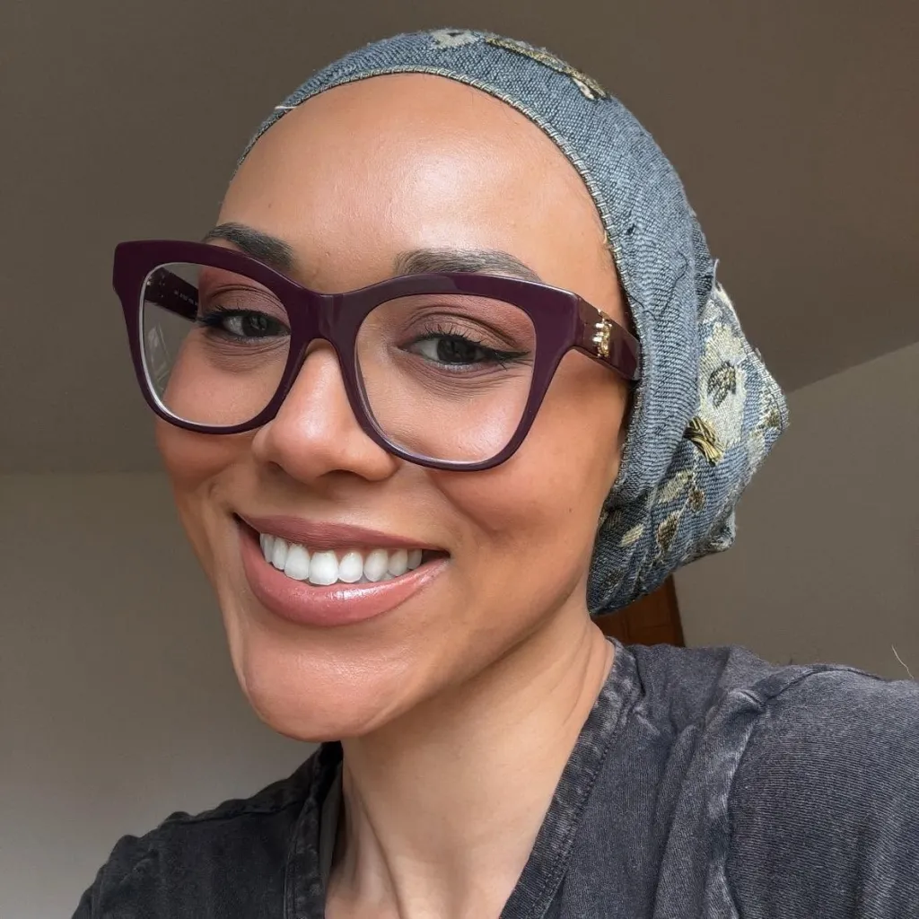 McKenna West smiling while wearing glasses and a head covering.