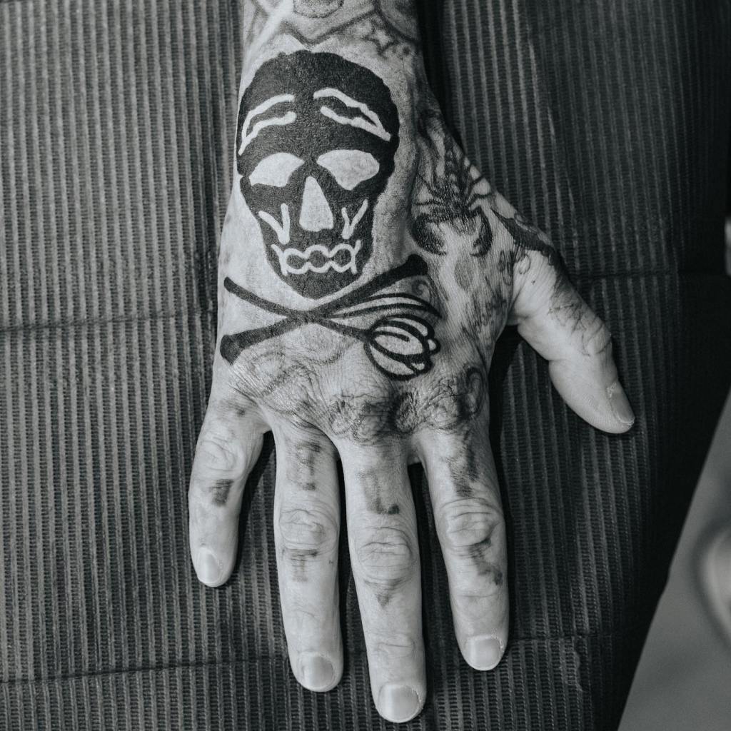 A hand covered in tattoos, including a large skull design with crossed bones or flowers on the back of the hand.