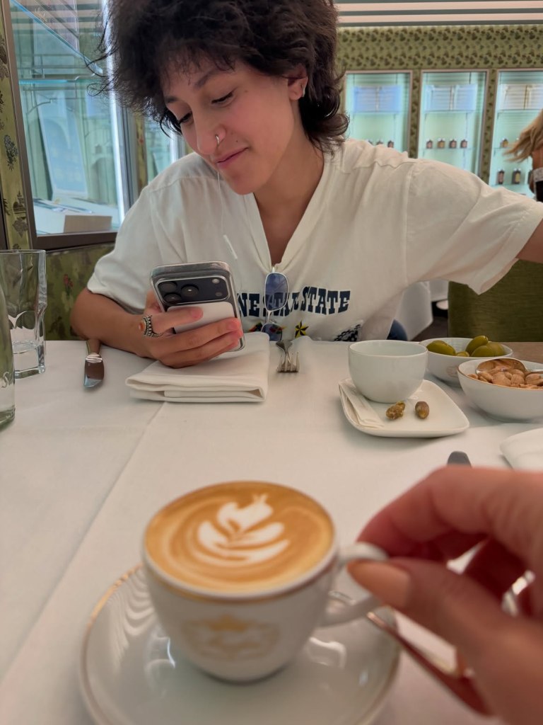 Jennifer Lopez's child Emme Muñiz looking at her phone at a restaurant in Italy.