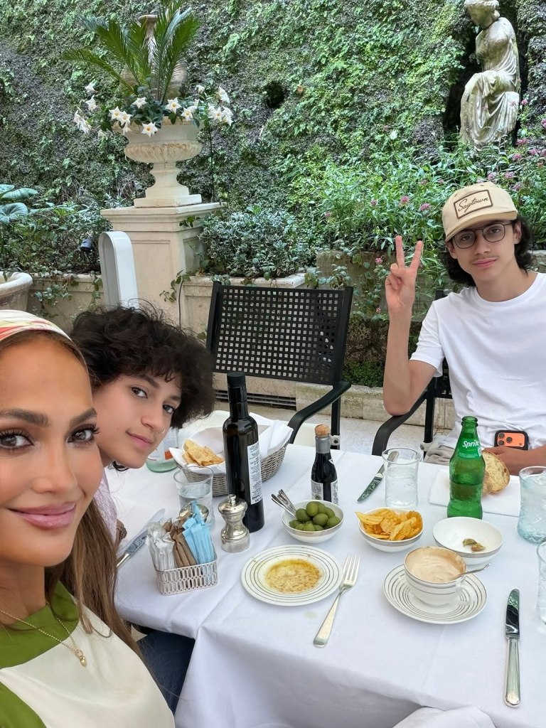 Jennifer Lopez taking a selfie with her twins Emme and Max at an outdoor restaurant in Italy.