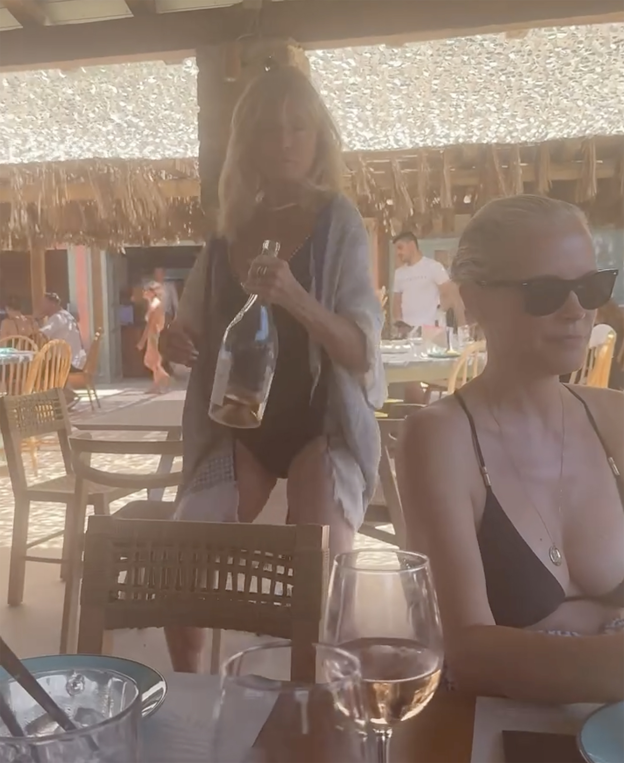 Goldie Hawn walking in a restaurant while holding a bottle of wine.