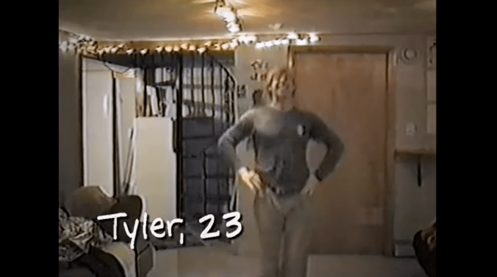 Video still of Tyler Duckworth posing with hands on hips, with white text overlay 
