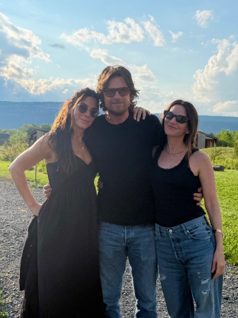 Sandra Bullock, a man, and Courteney Cox stand outdoors with their arms around each other.