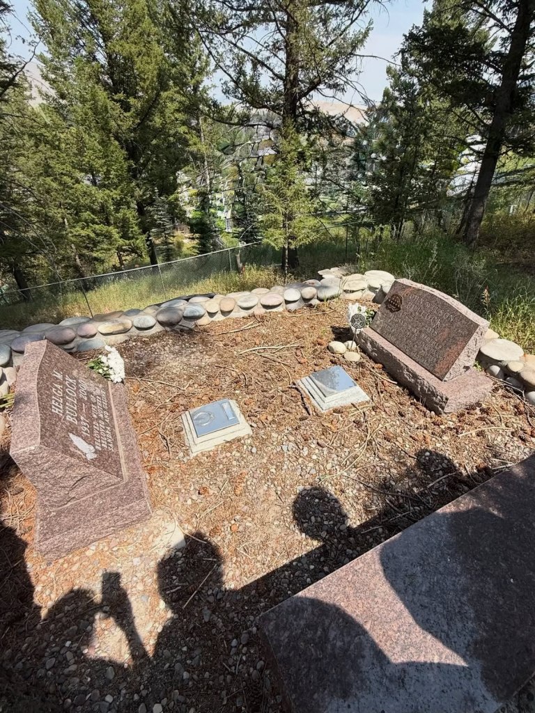 Gravesite of Helga M. Bullock and John Wilson Bullock, with two other smaller markers, surrounded by trees and a wire fence.