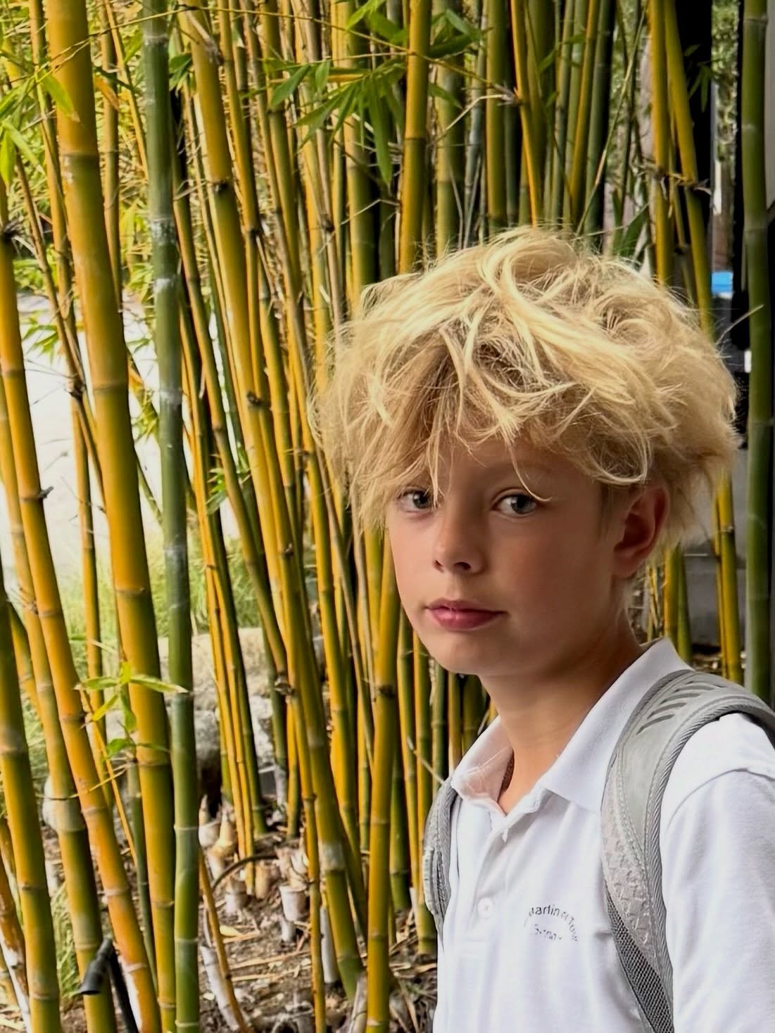 Axl Duhamel, son of Fergie and Josh Duhamel, standing in front of bamboo.