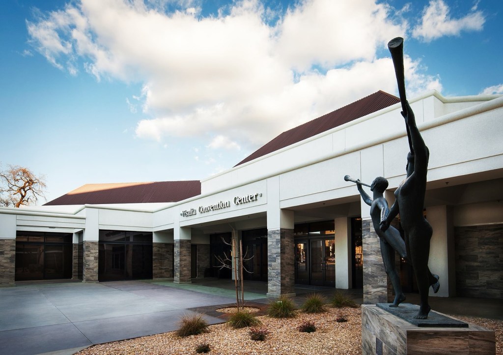 Exterior of the Visalia Convention Center with a sculpture of two figures with trumpets in the foreground.