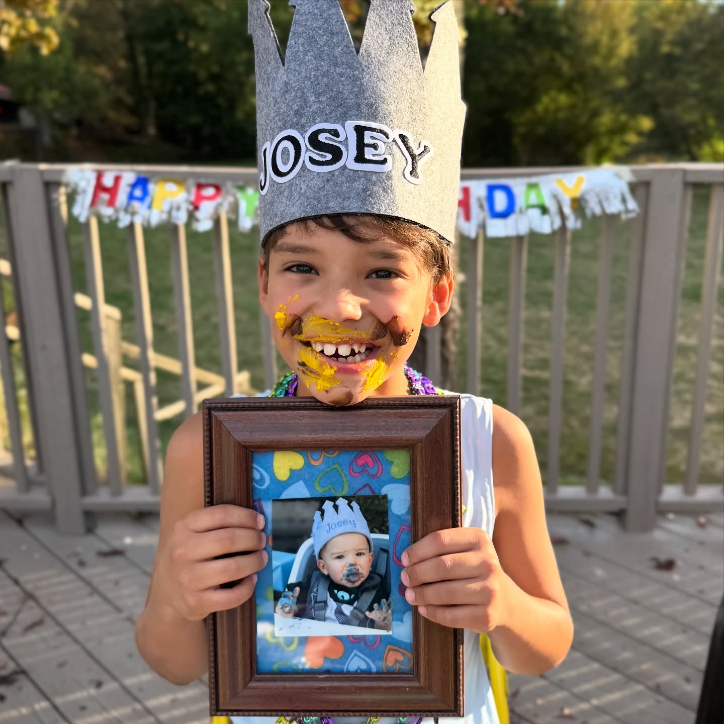 Josey Dorsey, wearing a crown with his name and cake on his face, holds a framed photo of himself as a baby also wearing a crown.