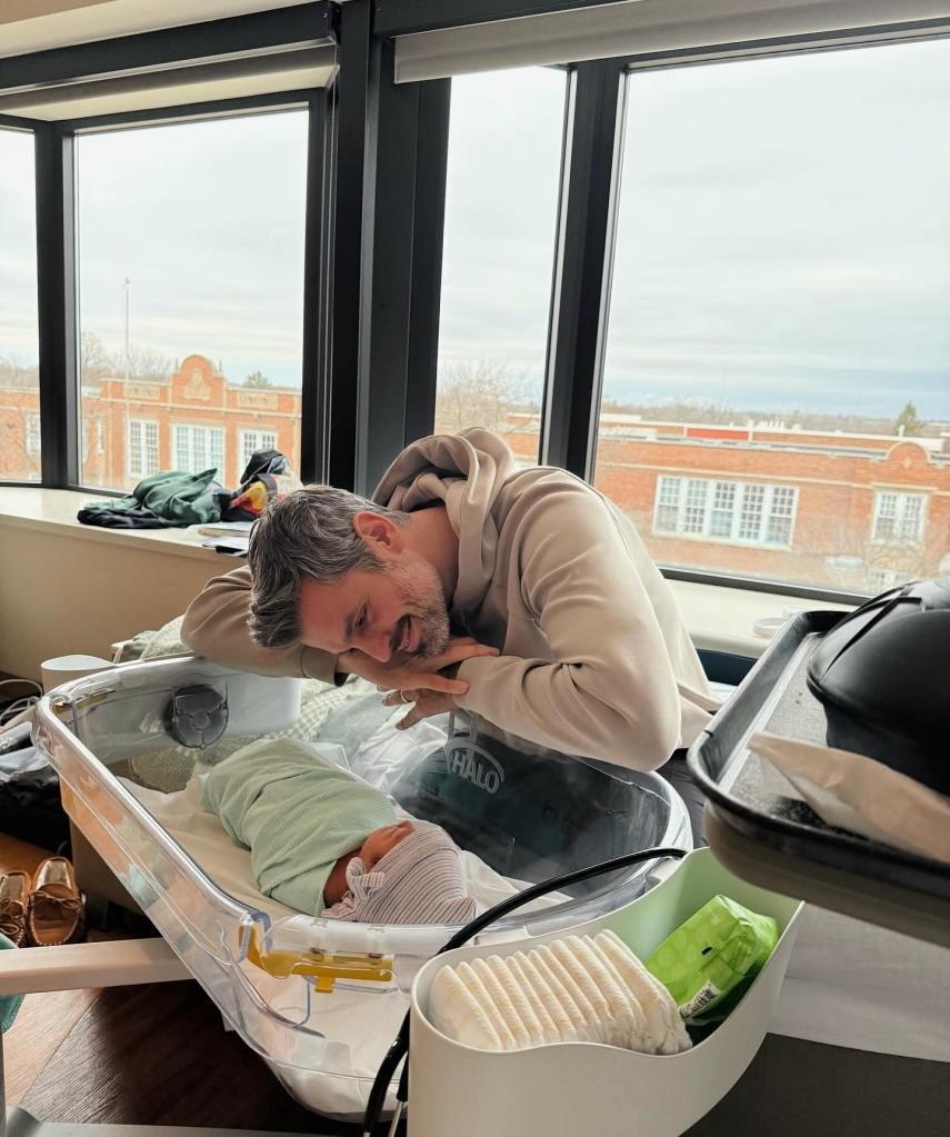Peter Kraus leaning over a hospital bassinet, smiling at his newborn baby.