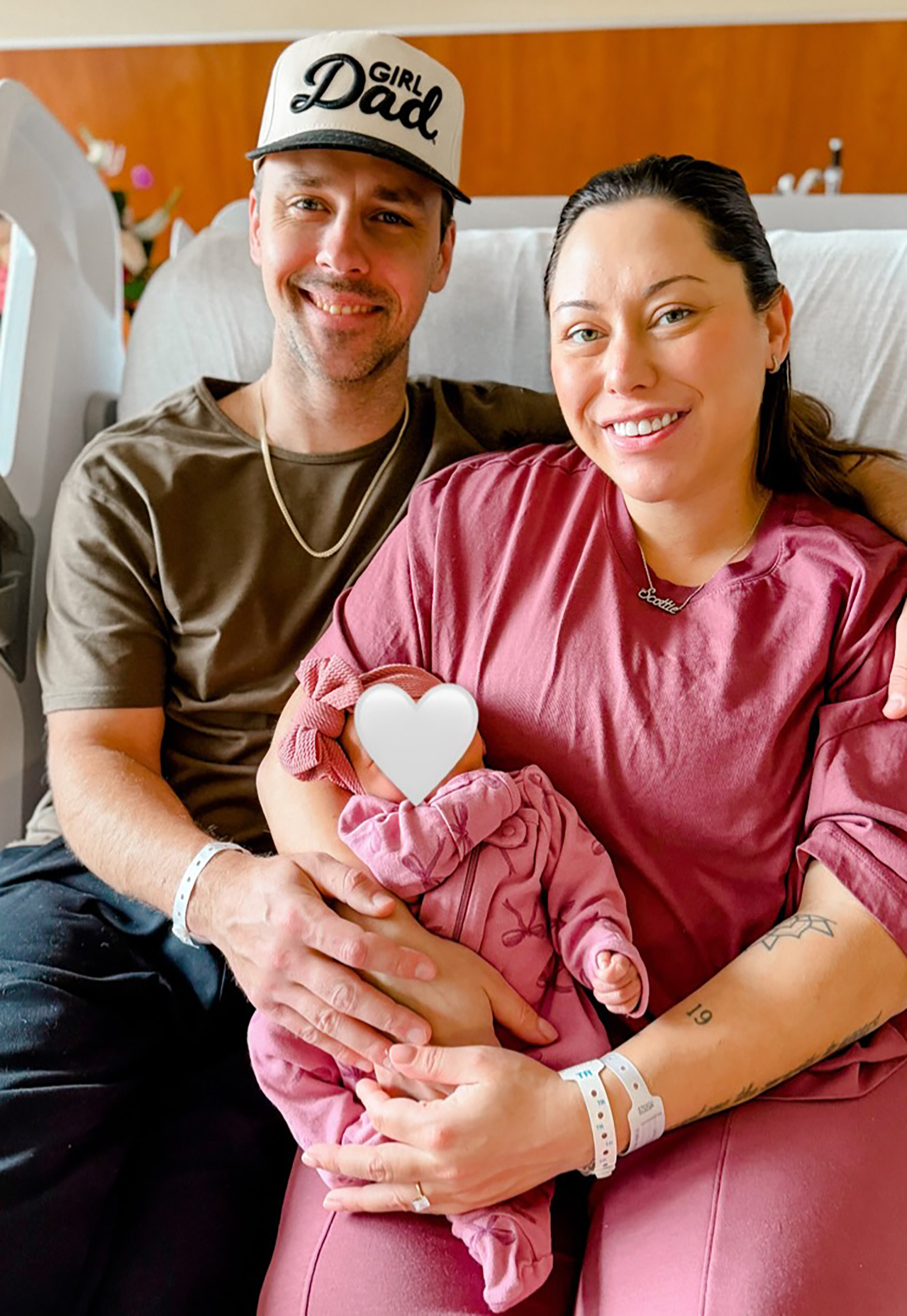 Alaina Scott and her husband, with their newborn daughter whose face is obscured by a white heart emoji.