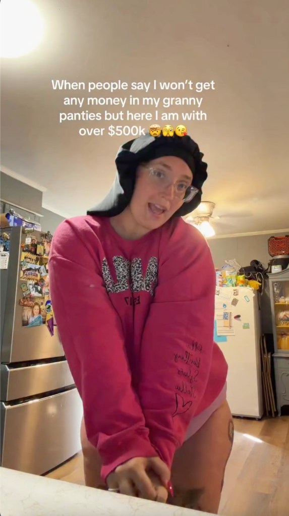 A woman wearing a pink sweatshirt and black bonnet, standing in a kitchen, with text overlay: 