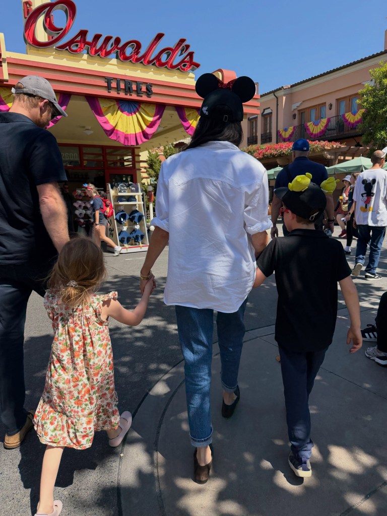 Meghan Markle, Prince Harry, and their two children, Prince Archie and Princess Lilibet, walk away from the camera in a theme park.