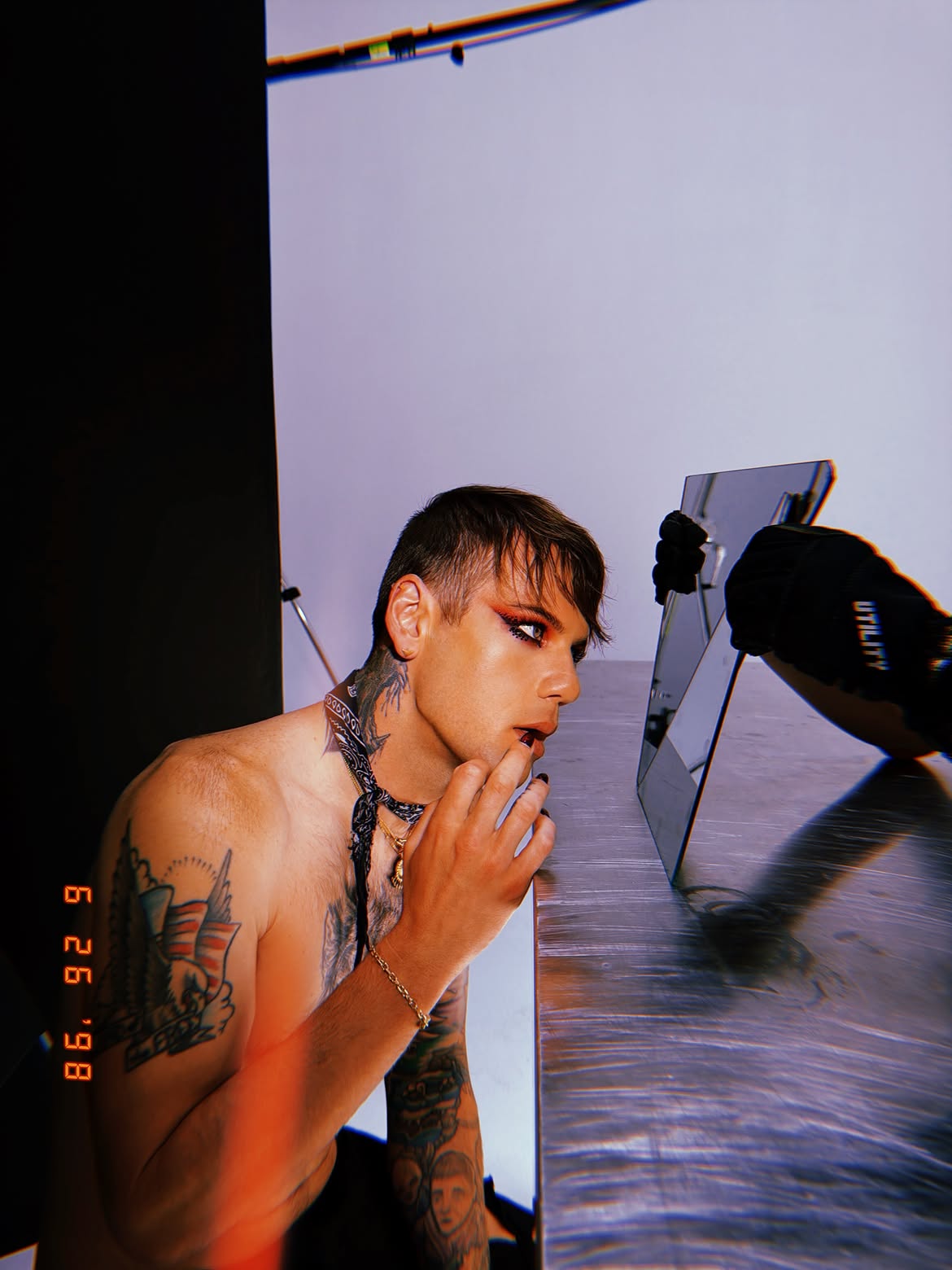 Caleb Shomo applying dark lipstick and red eyeshadow while looking into a mirror.
