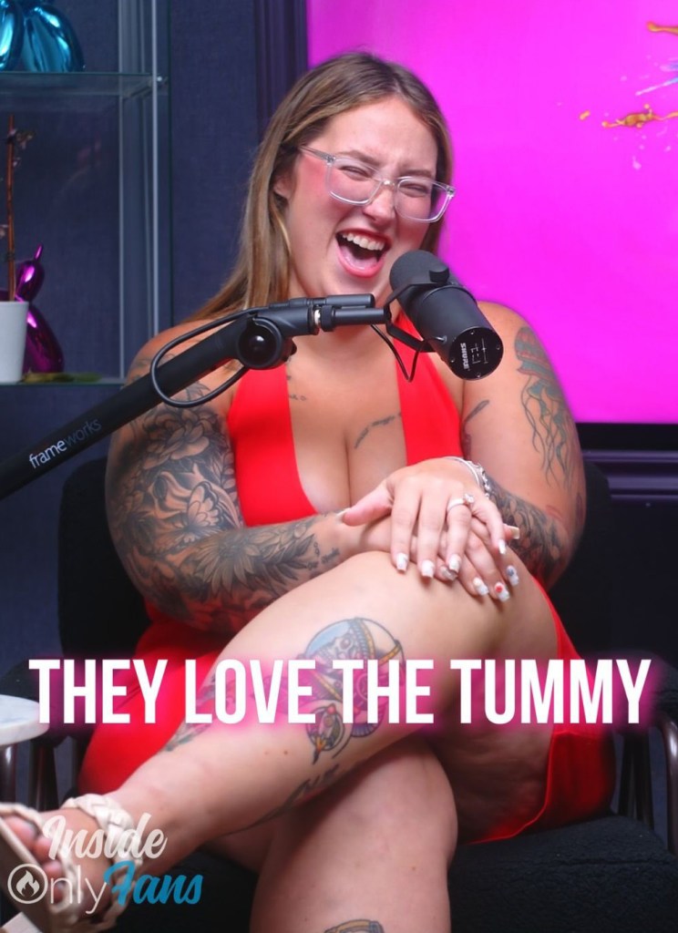Woman in a red dress with tattoos laughing into a microphone.