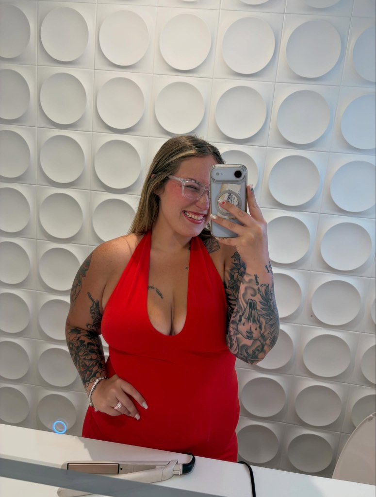 A woman in a red halter dress takes a mirror selfie.