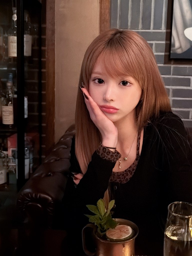 K-pop influencer Mina Chan resting her chin on her hand, sitting at a table with drinks.