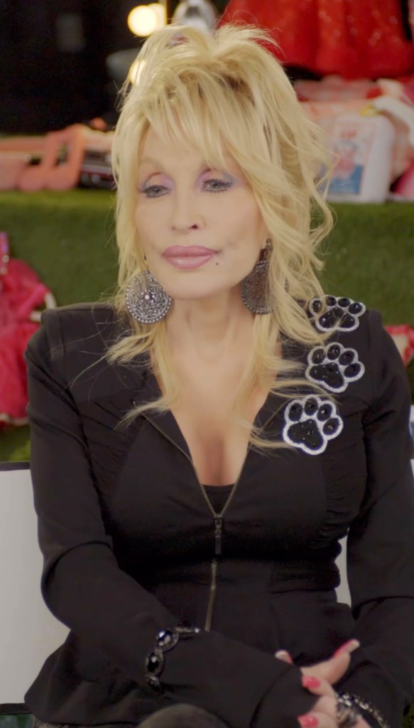 Dolly Parton wearing a black jacket with paw print embellishments and large earrings.