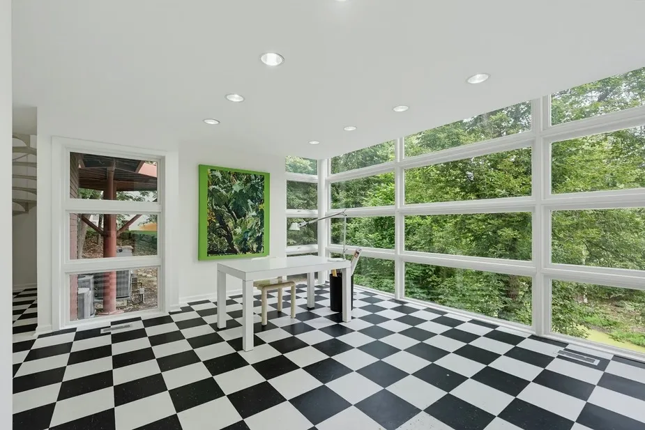 Interior of the Kenneth Neumann Upside-Down House, showing a white room with a black and white checkered floor and large windows looking out into green trees.