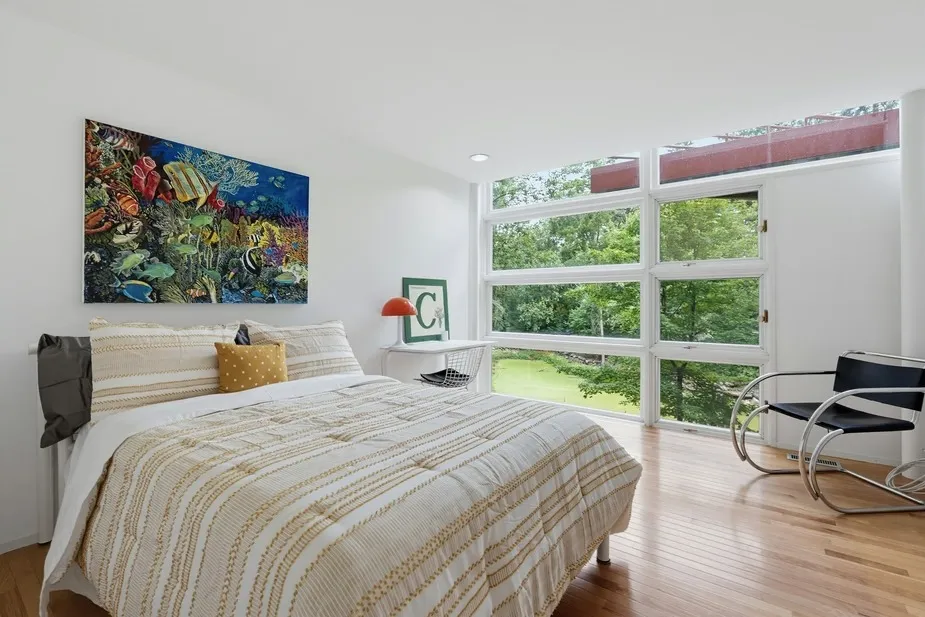 Bedroom with large windows overlooking a green landscape and a painting of fish and coral above the bed.