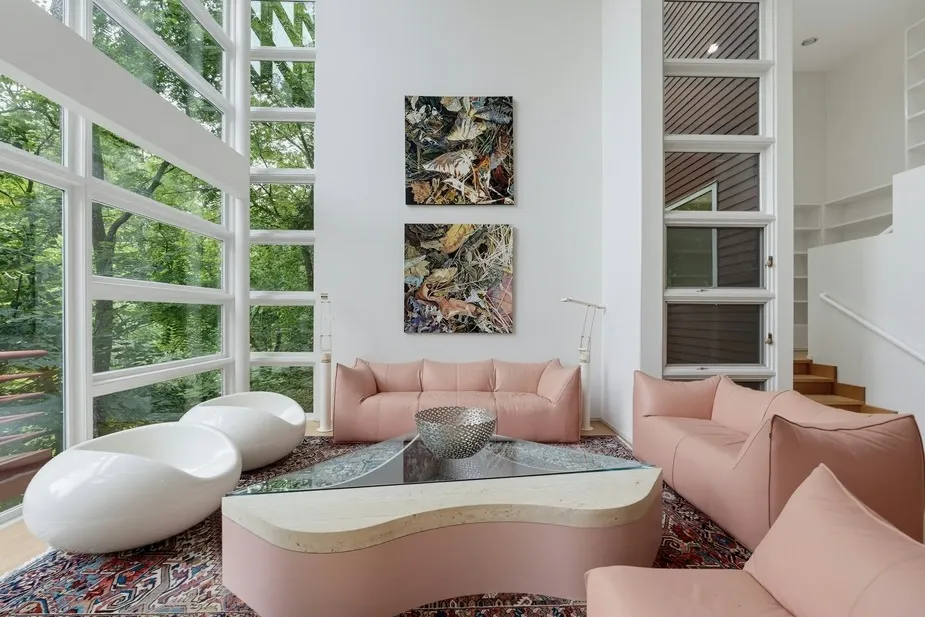 Living room in an upside down house designed by architect Kenneth Neumann, featuring large windows, pink sofas, a curved coffee table, and two white chairs.